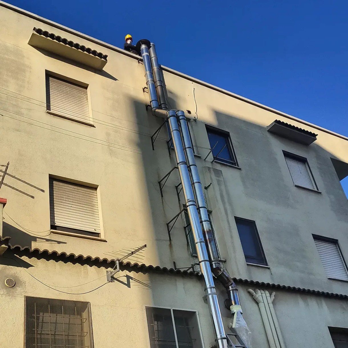 Spazzacamino sul tetto accanto a due canne fumarie in acciaio inox sulla facciata di un edificio