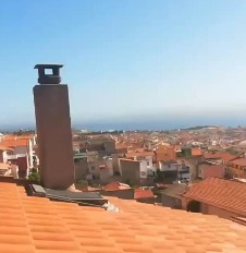 Comignolo in mattoni che sporge sopra il tetto, con il paese e il mare sullo sfondo