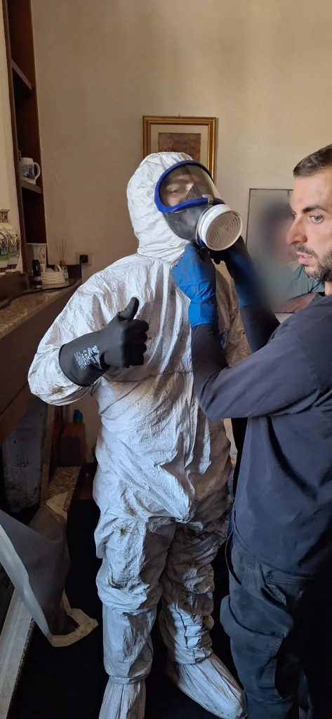 Spazzacamino in tuta protettiva e maschera a pieno facciale con il collega che lo aiuta a prepararsi