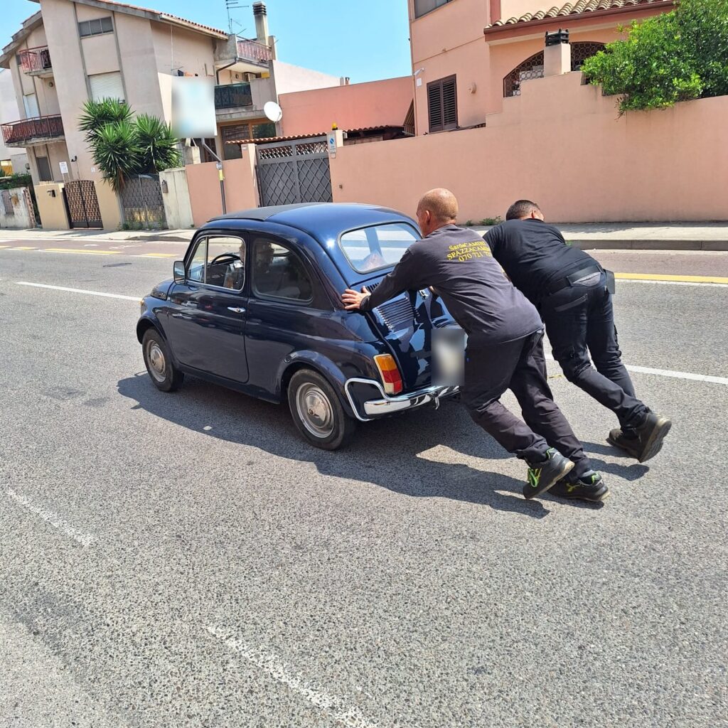 Due spazzacamini SardaCAMINI spingono una Fiat 500 d’epoca in strada