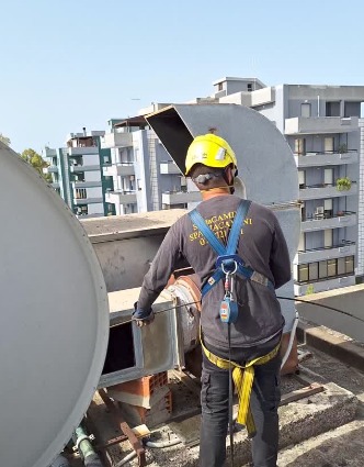 Spazzacamino con casco e imbracatura al lavoro su un torrino sul tetto di un palazzo