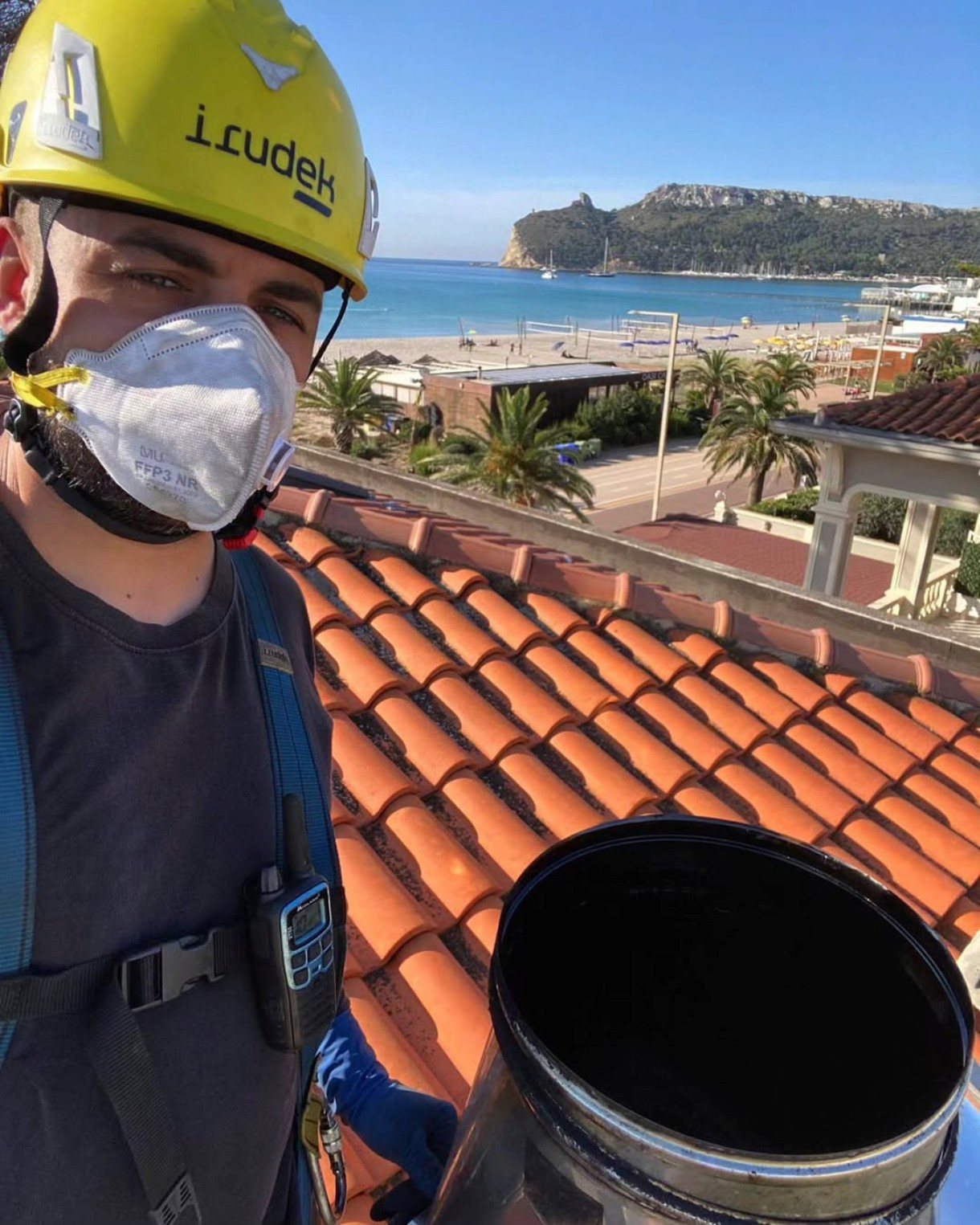 Spazzacamino con casco, mascherina e imbracatura sul tetto accanto a un comignolo